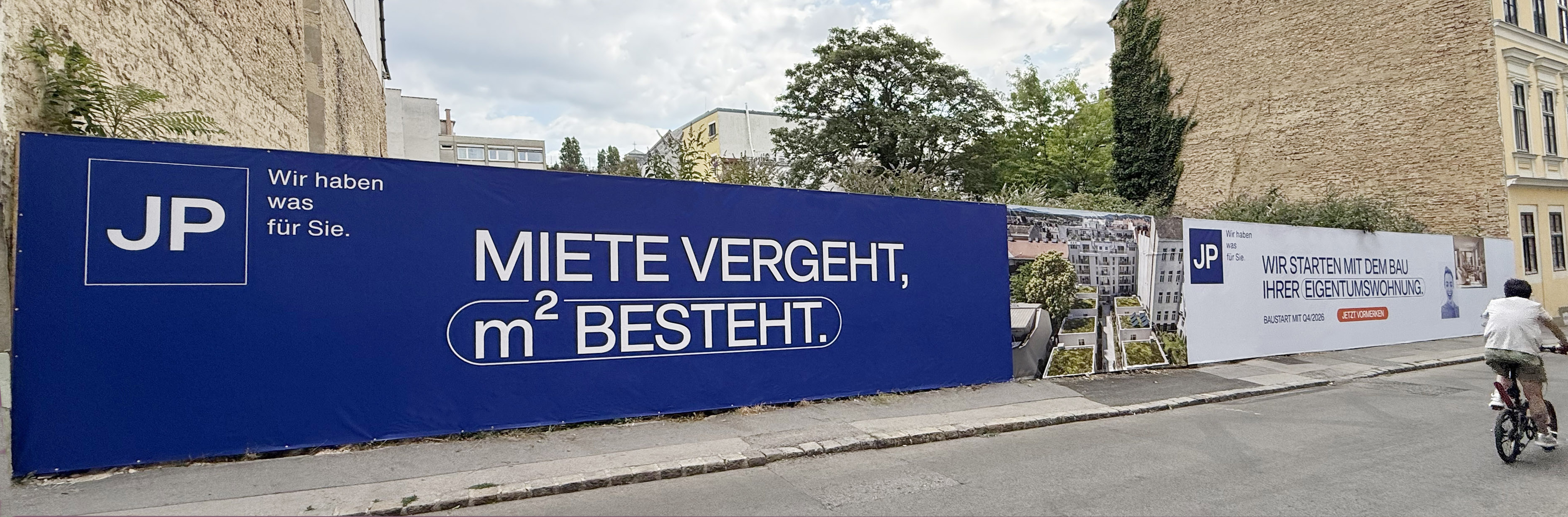 Großflächige Baueinhausung mit bedruckter Werbeplane für JP Immobilien